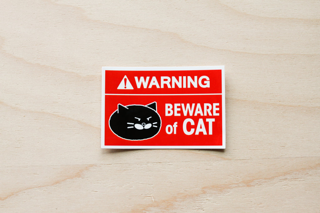 Warning sign with a cat illustration on a wooden surface