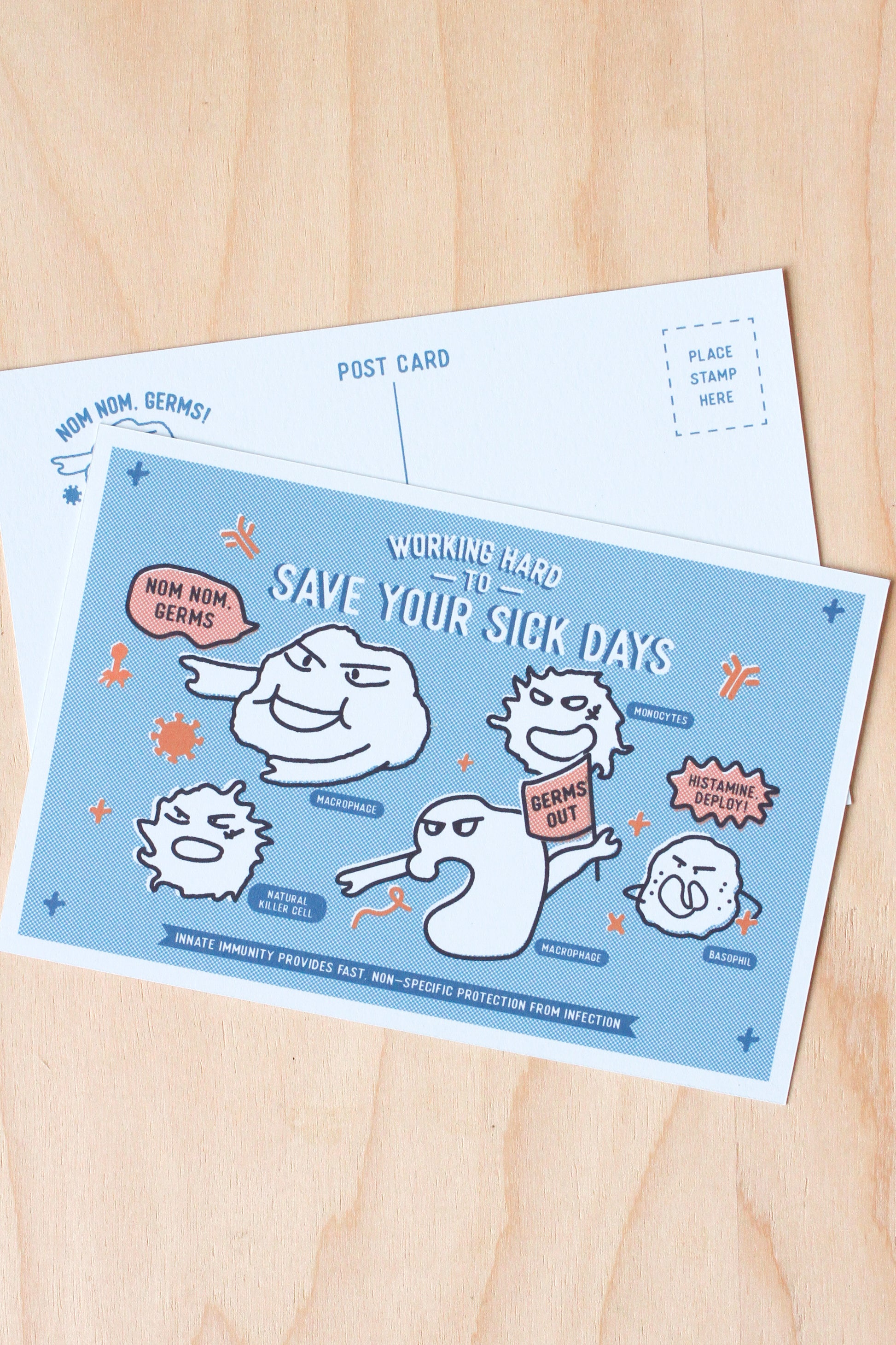 A postcard featuring a light blue background with cartoon germ characters and the text 'WORKING HARD TO SAVE YOUR SICK DAYS,' placed on top of a white postcard on a light wood surface.